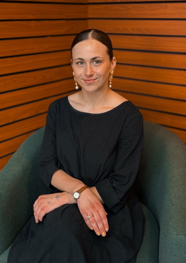 A female therapist sitting in a green chair in a wood paneled room.