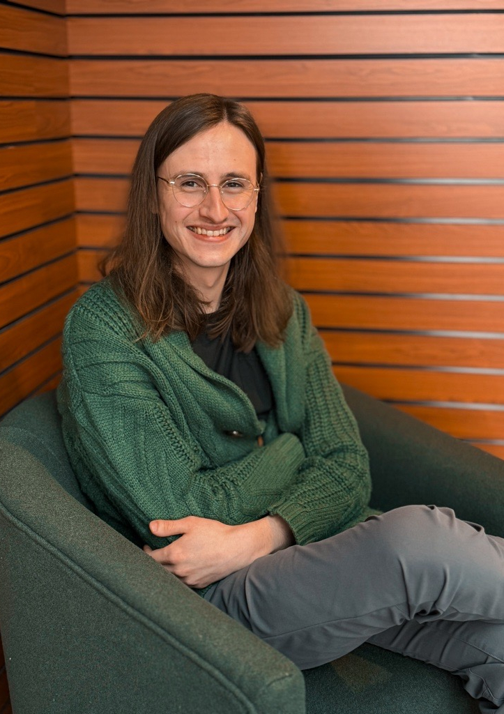 A male therapist sitting in a green chair in a wood paneled room.