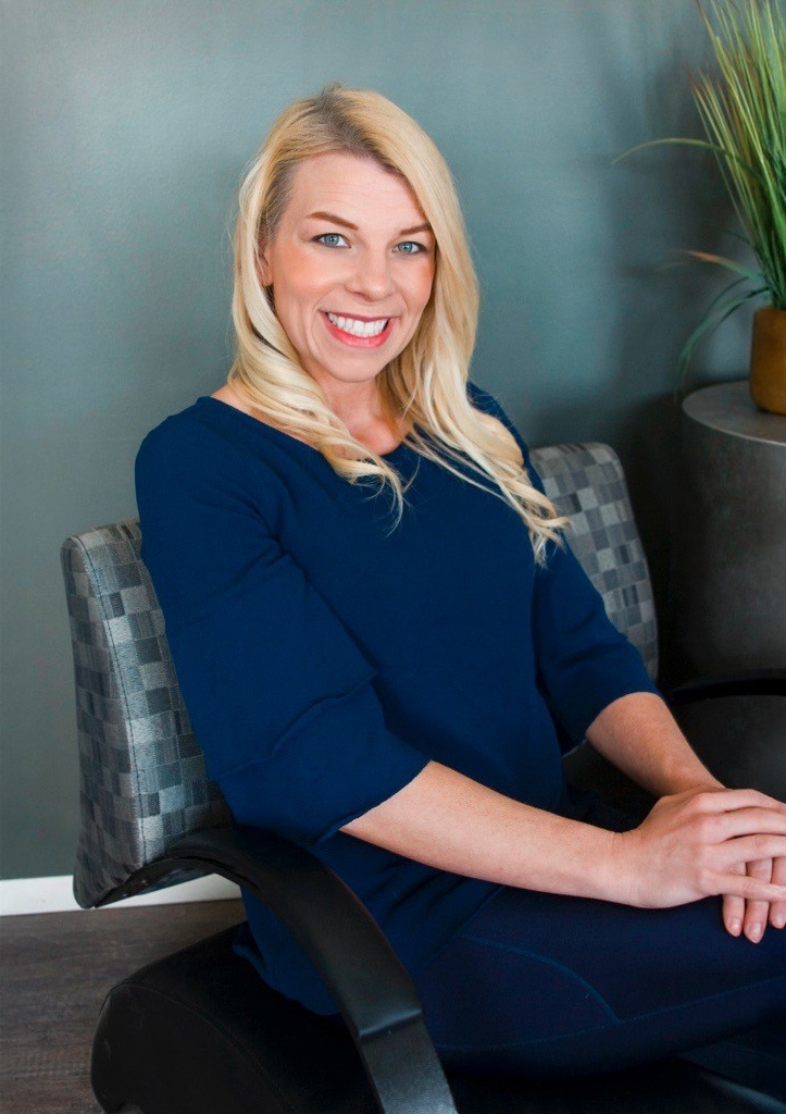 A female clinician sitting in front of a blue wall for a headshot.
